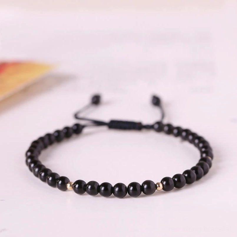 Black obsidian 4mm beaded red string bracelet with gold accents, flat lay view on light surface