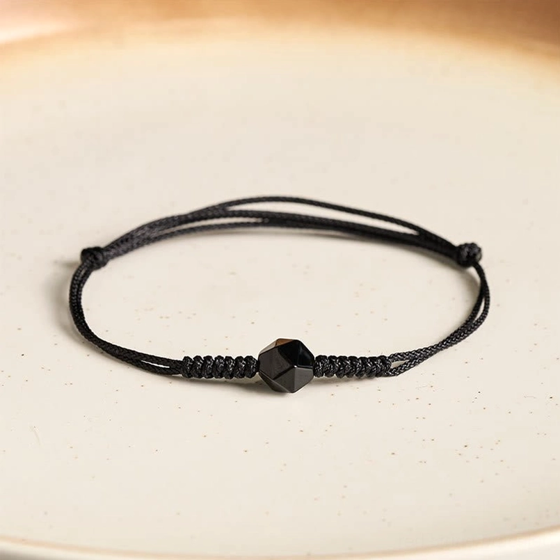 Minimalist black obsidian protection bracelet with braided knot on ceramic plate flat lay