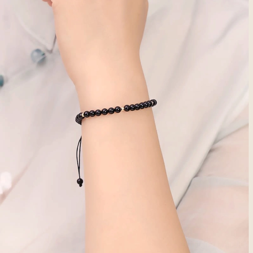 Thin black obsidian beaded bracelet worn on wrist front view with long hanging cord tails