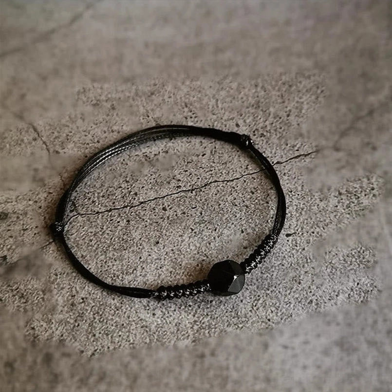 Black obsidian strength bracelet with neat woven knot and faceted bead on cracked concrete