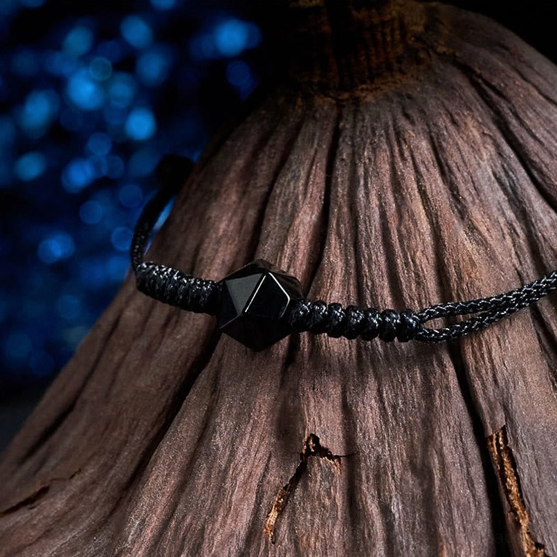 Black obsidian braided cord bracelet side angle view with faceted bead on dark wood