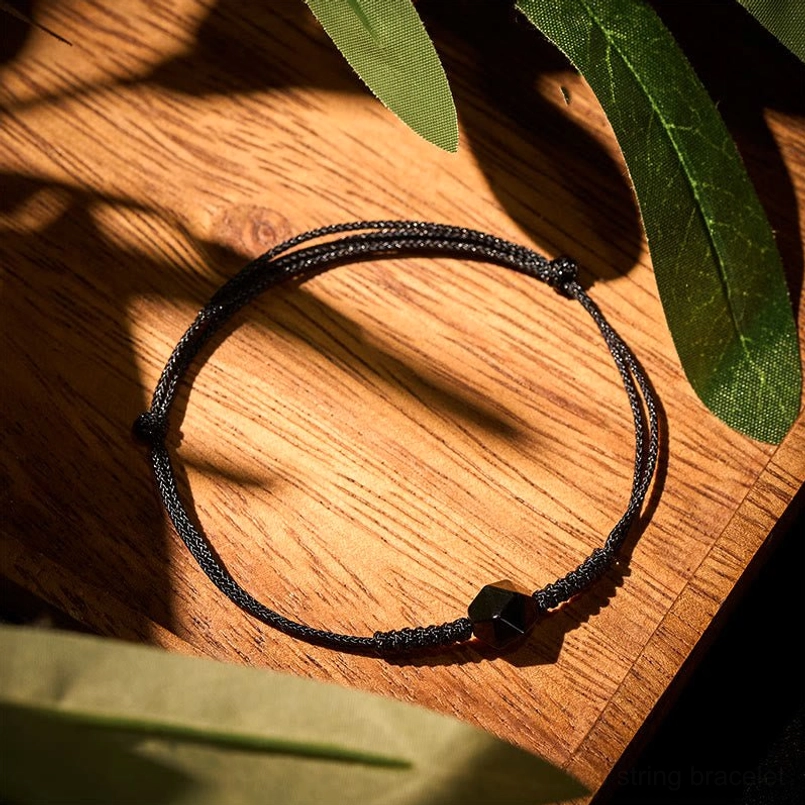 Black obsidian braided strength bracelet with faceted bead on wooden surface with green leaves