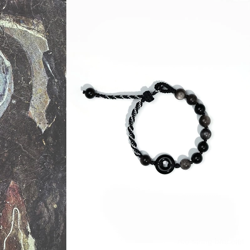 Black obsidian peace buckle bracelet with adjustable braided rope, flat lay overhead view on vintage stone texture background