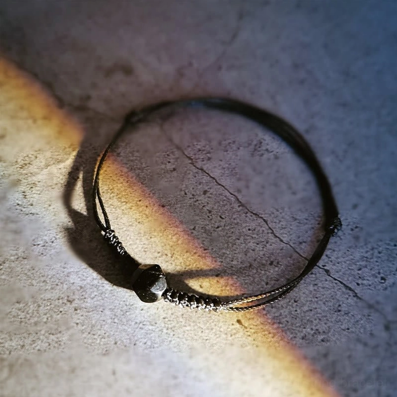 Black obsidian protection bracelet with faceted bead on cracked concrete surface