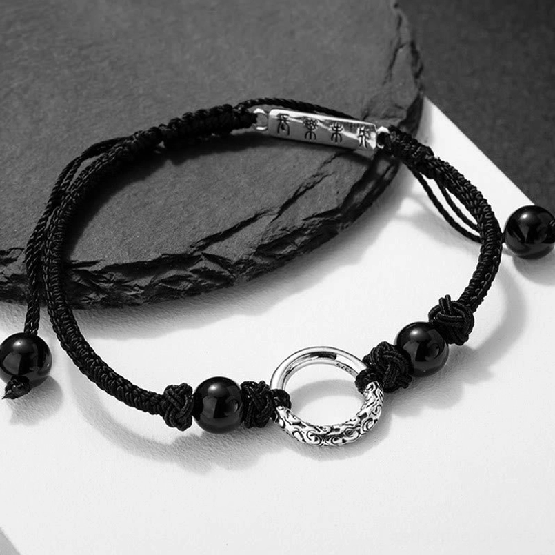Angled side view of 925 silver black onyx peace buckle bracelet on crumpled black paper