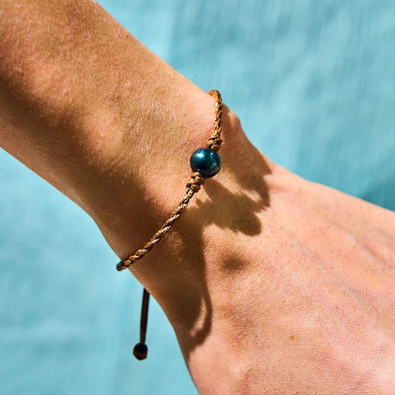 Tahitian black pearl protection bracelet worn on wrist - water background lifestyle shot