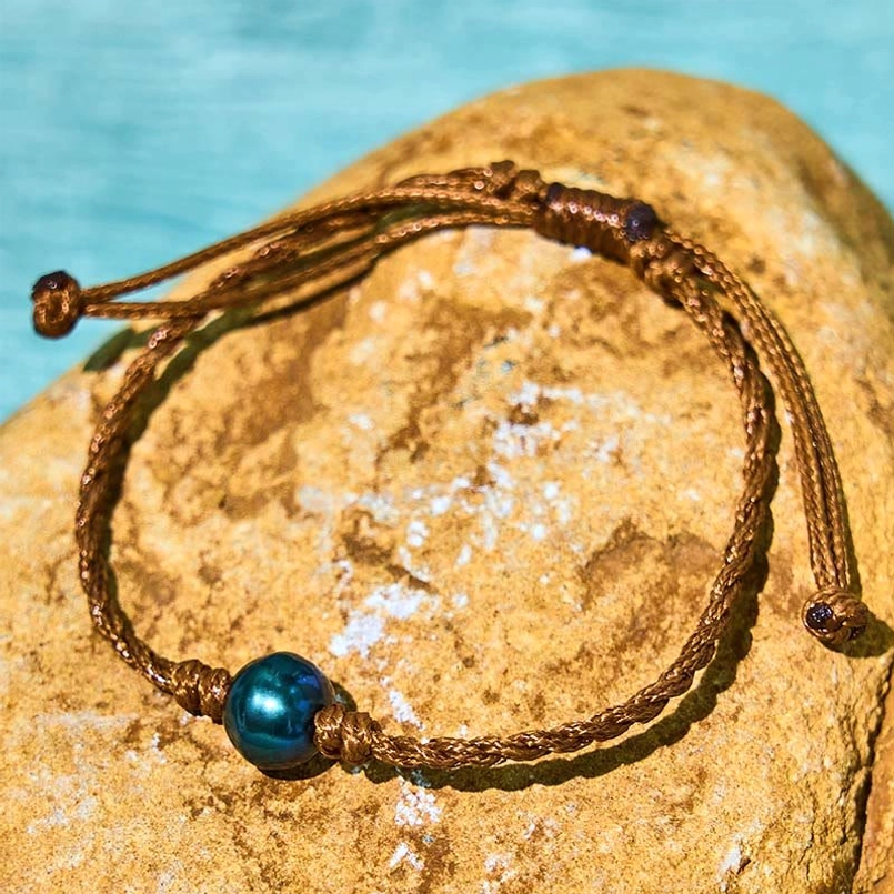 Black pearl wax rope bracelet close-up - braided cord and pearl detail on stone texture