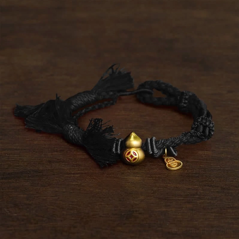 Black braided string bracelet with gold gourd coin charm on dark wooden background