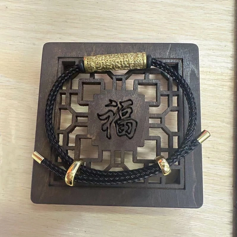 Black Tibetan string bracelet with gold metal embossed charm on traditional feng shui carved plaque