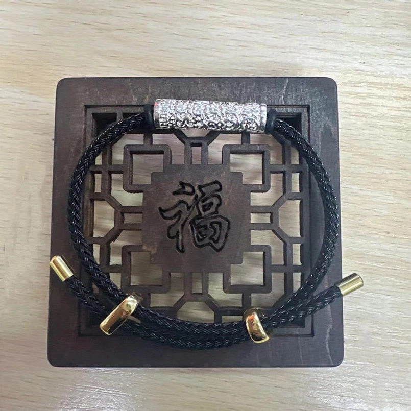 Black woven Tibetan lucky bracelet with matte engraved silver metal tube on wooden backdrop