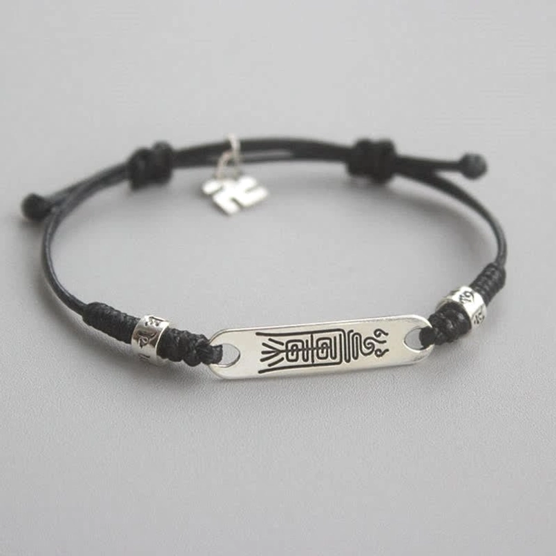 Black braided string silver bracelet with swastika charm and engraved silver plate, flat lay