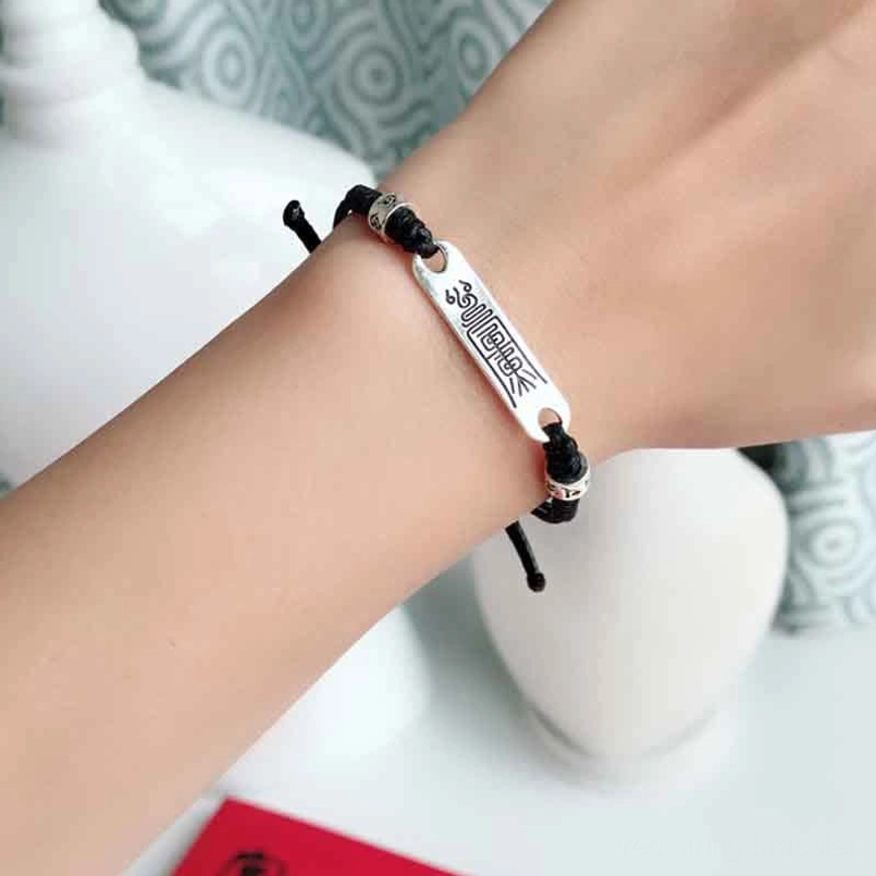 Black string silver wrist bracelet with engraved charm worn on female wrist, lifestyle view