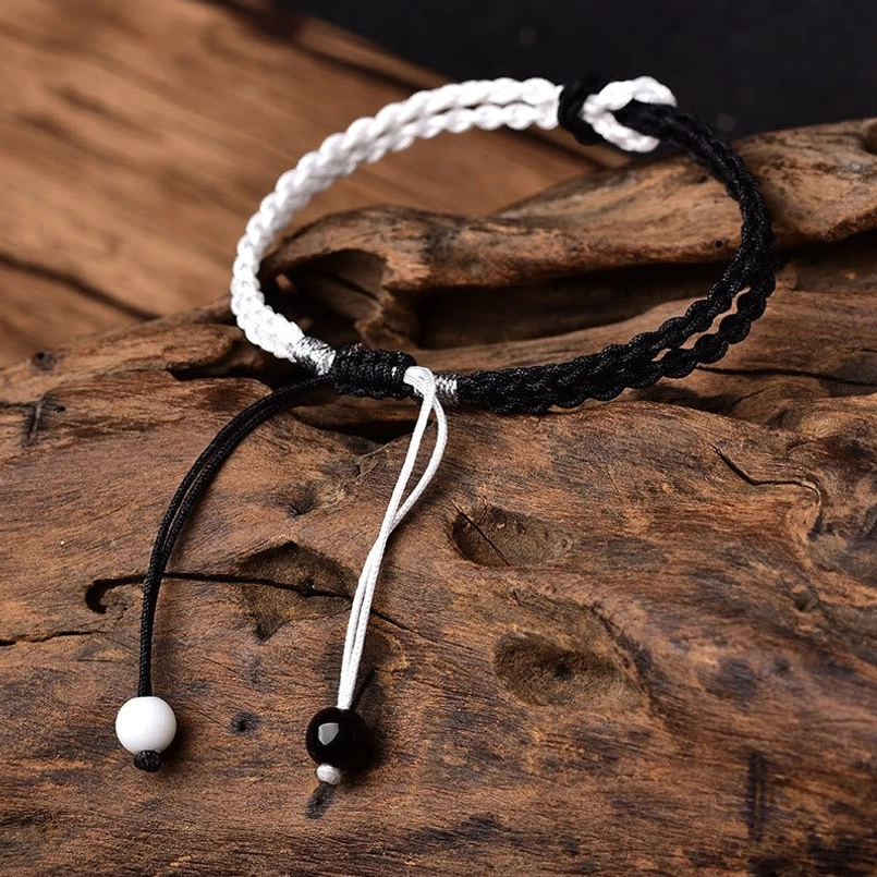 Black white braided healing bracelet side view showing adjustable tail cords and beads