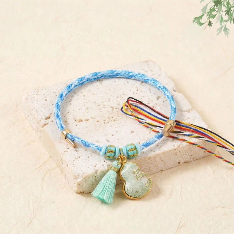 Light blue song brocade bracelet with colorful drawstrings mint tassel and gourd charm on stone background
