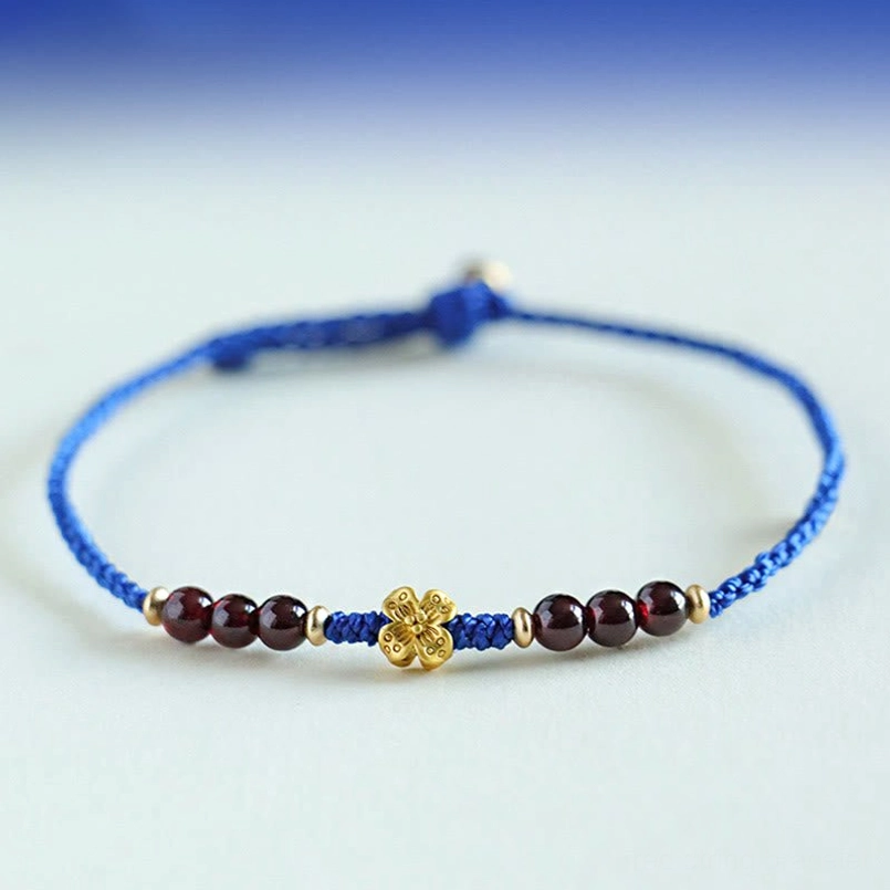 Blue braided garnet bracelet with copper clover charm flat lay on gradient blue background