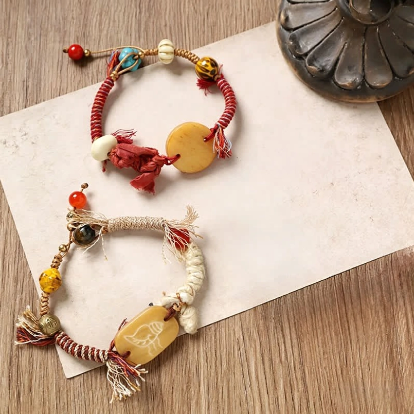 Three red and brown braided bone charm bracelets displayed together on craft paper
