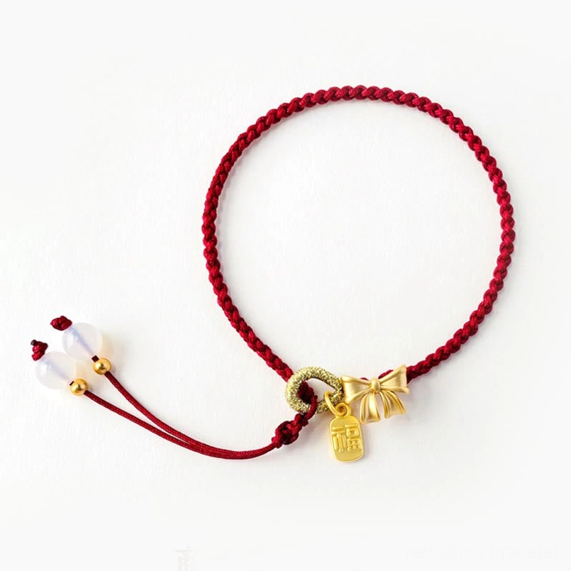Side overhead shot of red rope bracelet featuring gold bow charm, Fu pendant, and white bead adjuster