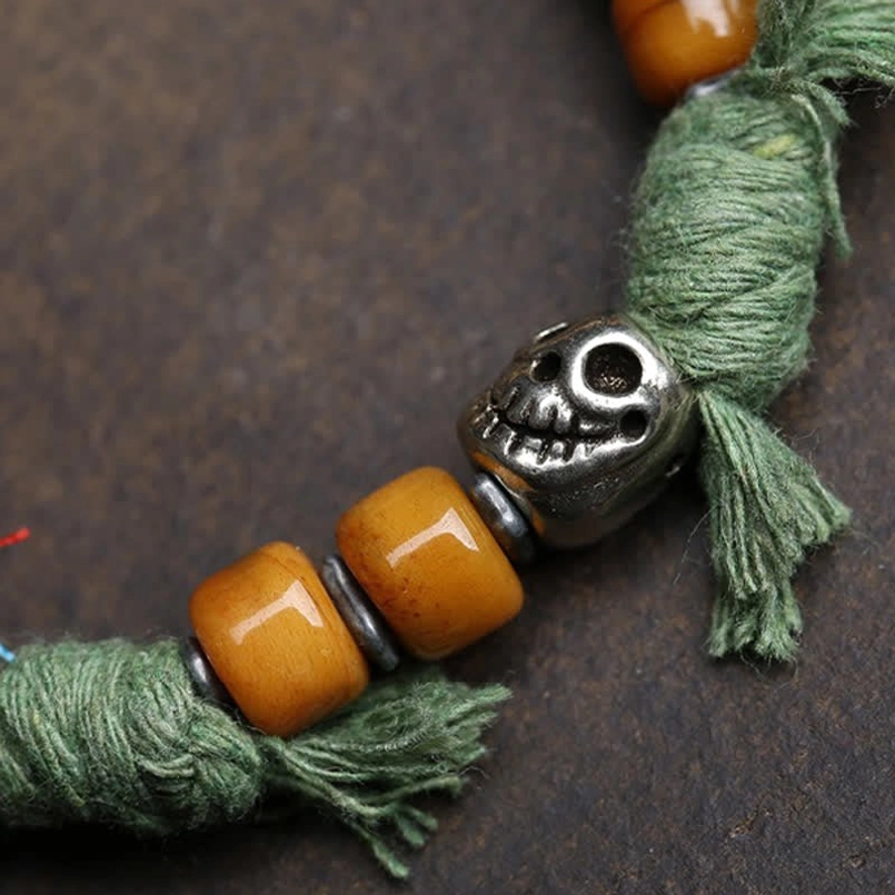 Carved silver bead and amber resin beads with green tassel on red cord