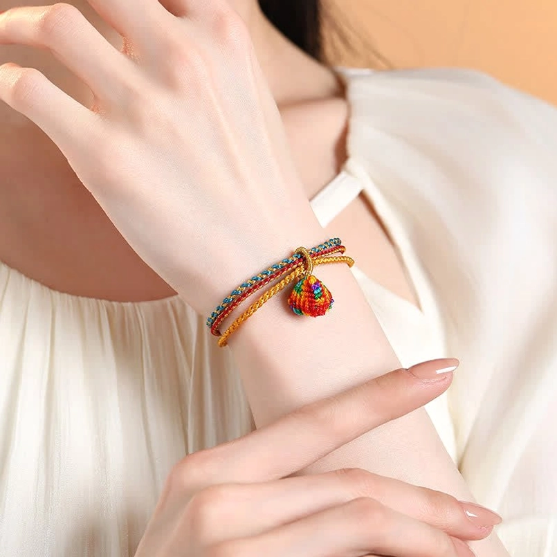 Woman wearing triple wrap braided bracelet with colorful zongzi charm pendant, wrist detail shot