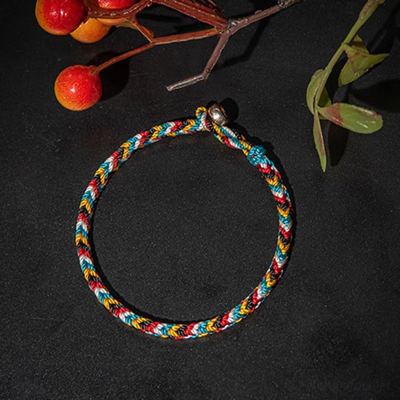 Tibetan five color protection red string bracelet top view on dark background with red berries