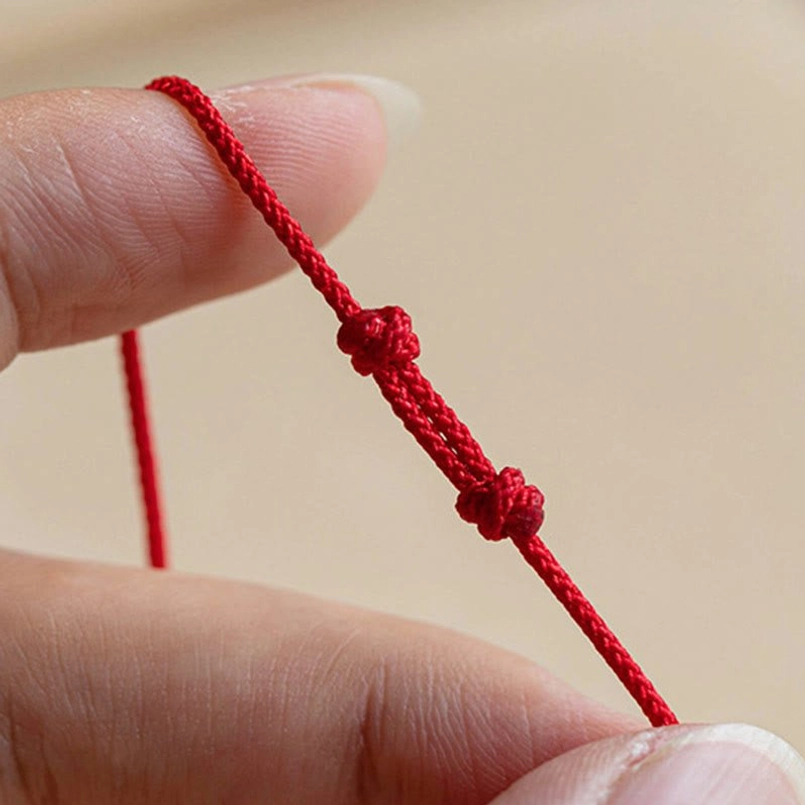 Close-up of ultra-thin braided red rope with decorative knots on fortune bracelet