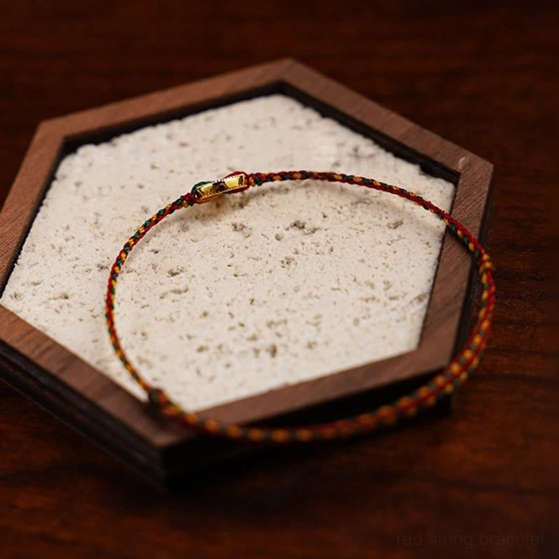 Adjustable red string bracelet with copper coin placed in hexagonal wooden display tray