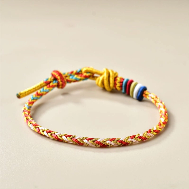 Low angle view of braided red string bracelet with gold toggle clasp on beige background