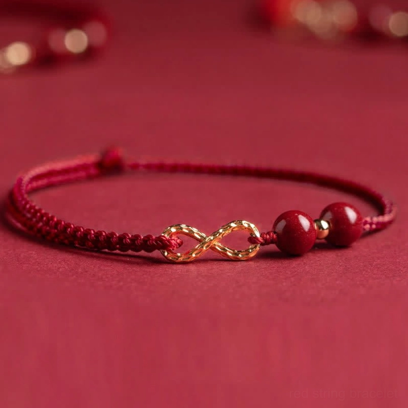 Braided red string infinity bracelet with gold charm and cinnabar beads, top-down flat lay product view