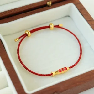 Brass koi fish red string wealth bracelet top view on wooden jewelry box