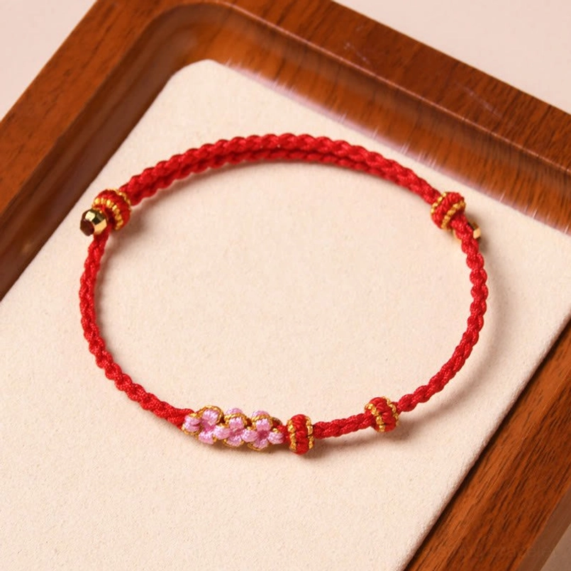 Bright red floral braided protection bracelet with peach blossom beads overhead view