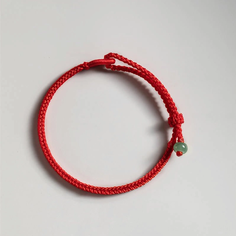 Flat lay of bright red string jade bracelet on plain light gray background