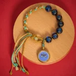 Five Directions Wealth God Buddha Eye glass bead bracelet in blue with gold accents, flat lay on wooden coaster