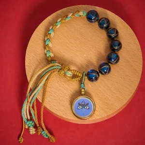 Five Directions Wealth God Buddha Eye glass bead bracelet in blue with gold accents, flat lay on wooden coaster