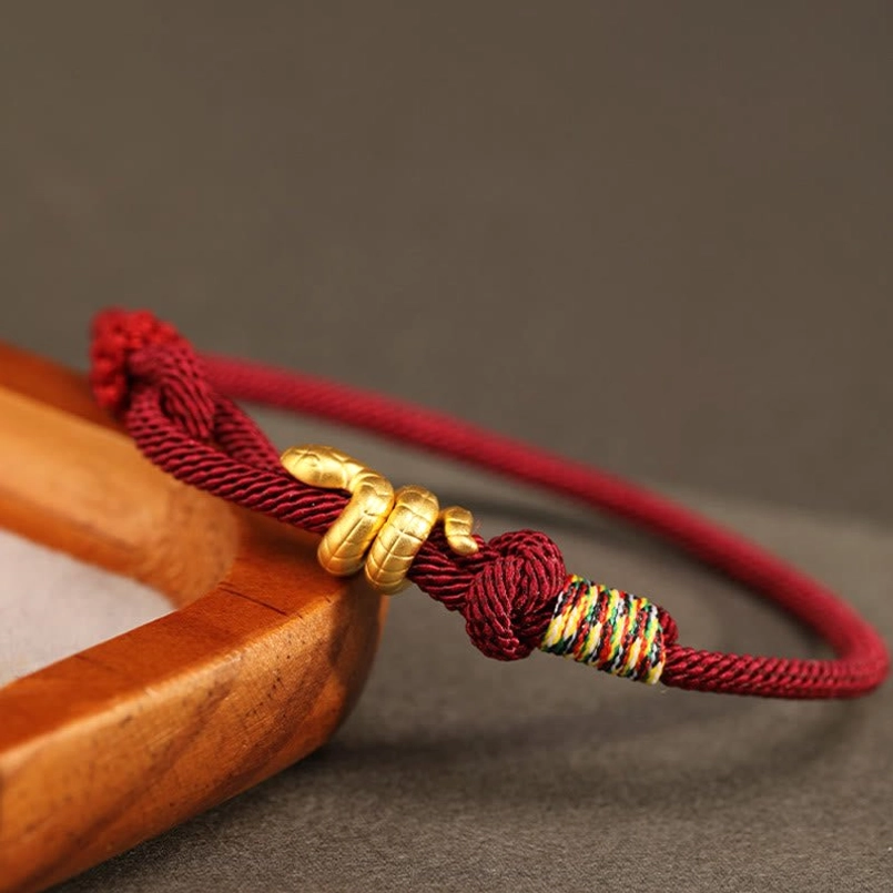 burgundy gold snake red string bracelet low side view on wooden edge