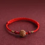 Carved peach wood lucky red rope bracelet close up view on maroon background