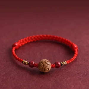 Carved peach wood lucky red rope bracelet close up view on maroon background