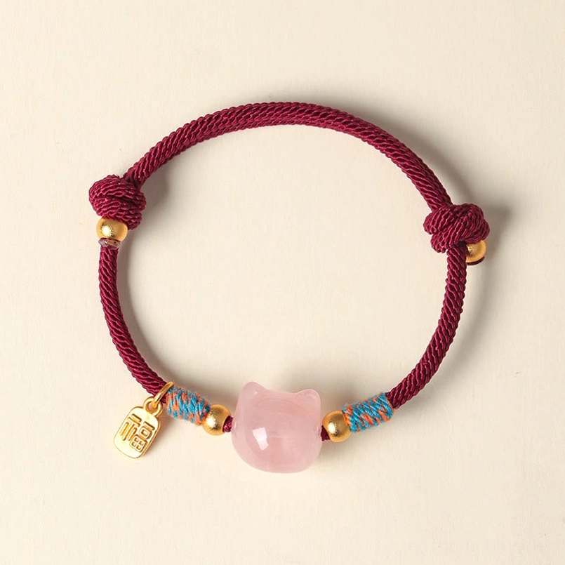 Direct top-down view of red braided cord cat bracelet with pink crystal cat bead and gold-toned Fu charm