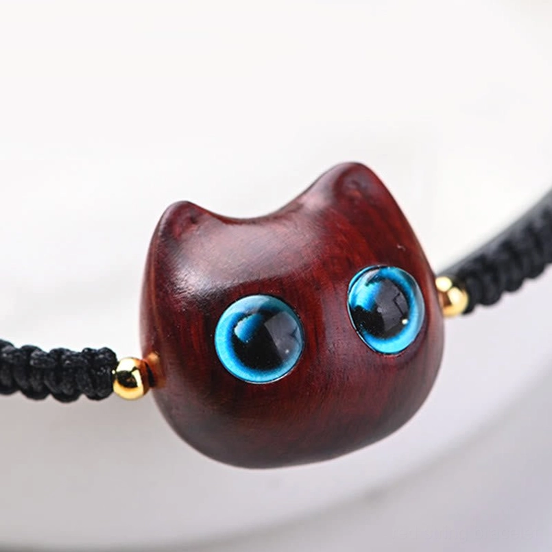 Handcarved wooden cat head charm close-up with blue glass eyes natural wood grain
