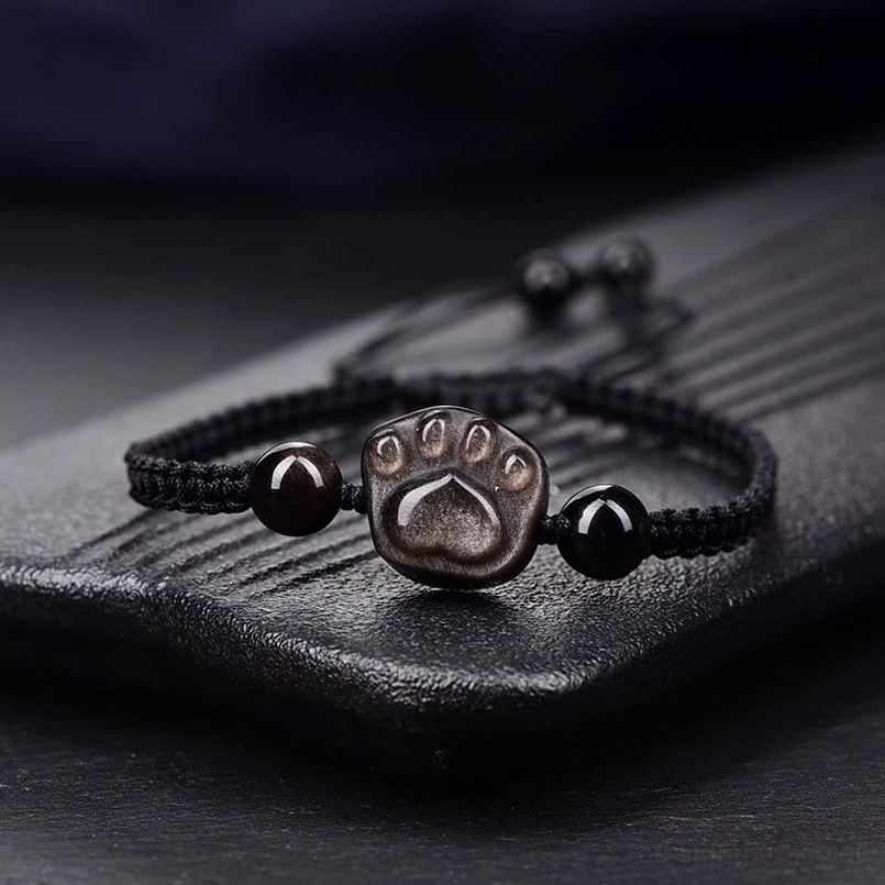 Black braided cat paw obsidian bracelet with silver charm wooden tray
