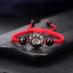 Red string cat paw obsidian protection bracelet with silver charm on wooden tray