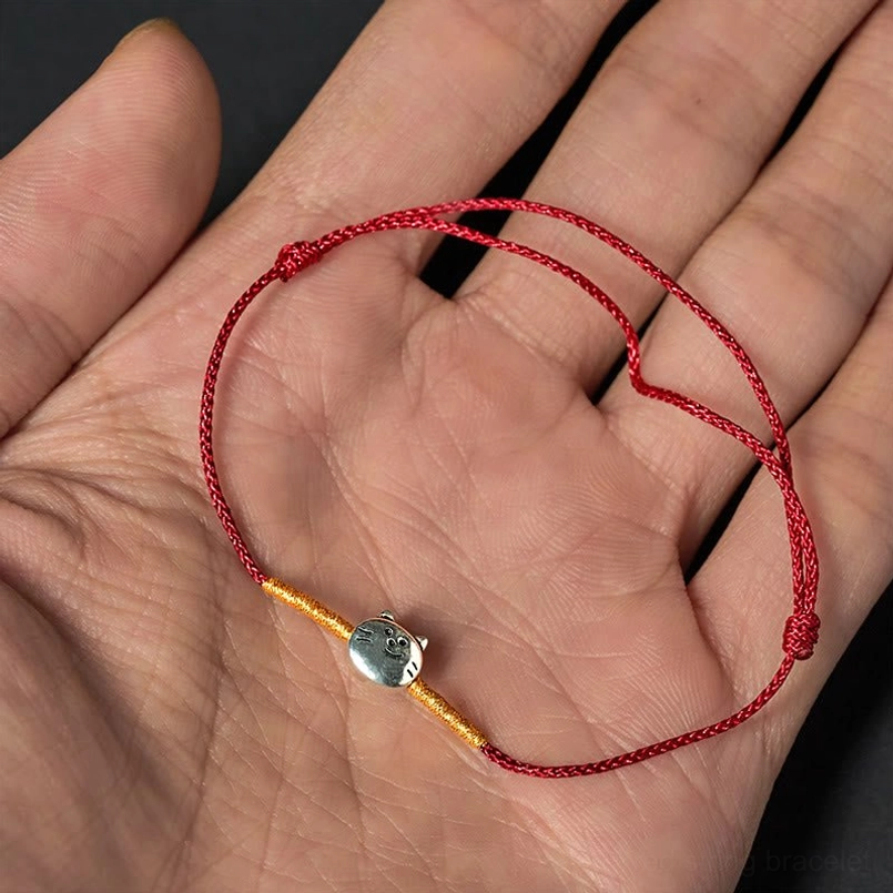 Adjustable red braided cat charm bracelet held in open palm with silver accents