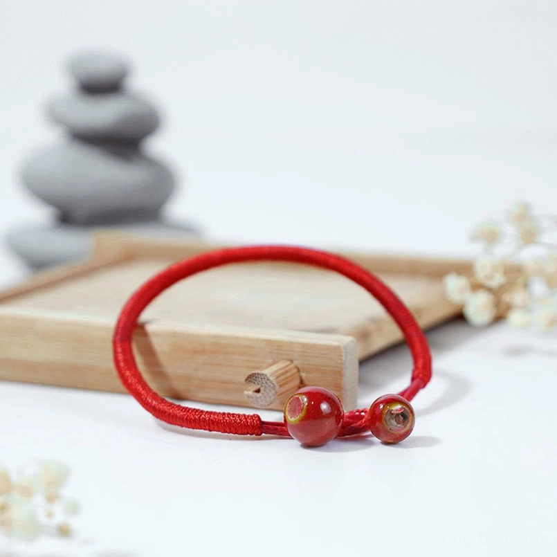 Low angle three-quarter view showing paired reddish-brown ceramic beads on red woven cord