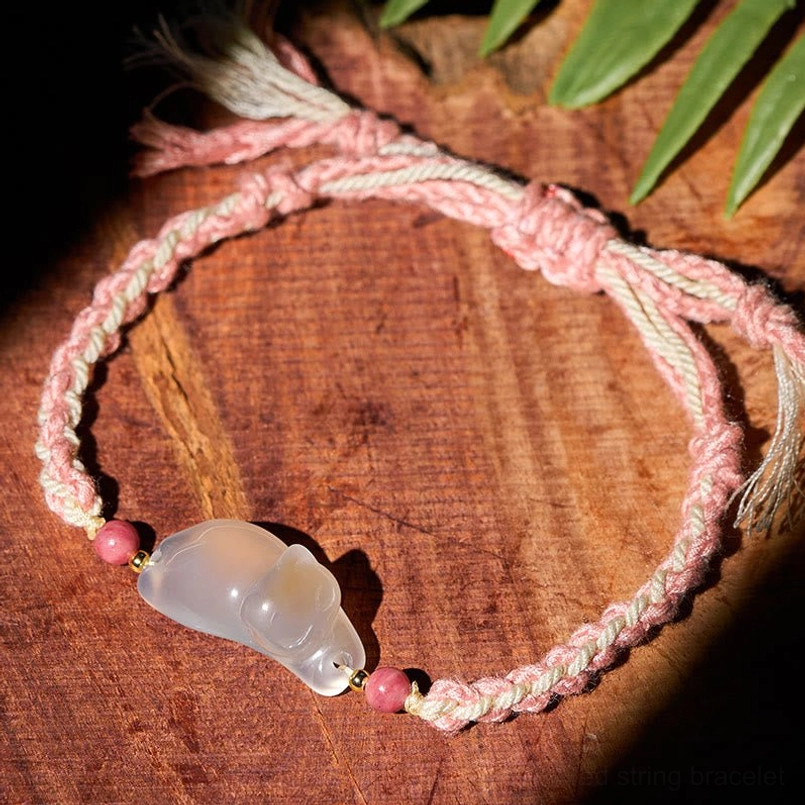 Top-down view of adjustable chalcedony cat bracelet with polished stone charm and braided knot