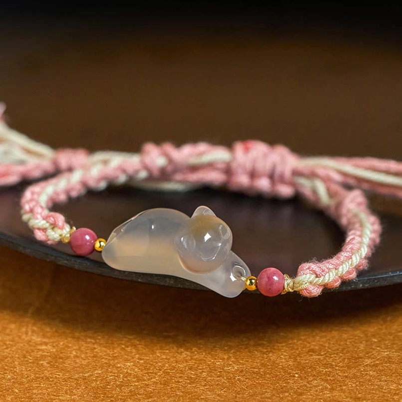 Close-up side view of chalcedony cat charm on woven cord bracelet with gold bead spacers