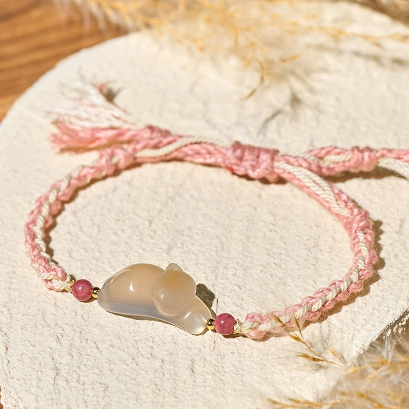 Flat lay overhead view of chalcedony cat bracelet with pink cotton rope and stone beads on linen mat