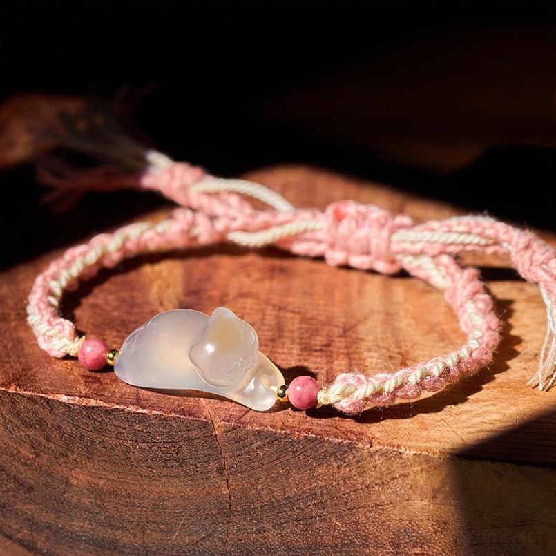 Chalcedony cat bracelet with pink braided string on wooden surface, showing adjustable knot and stone pendant