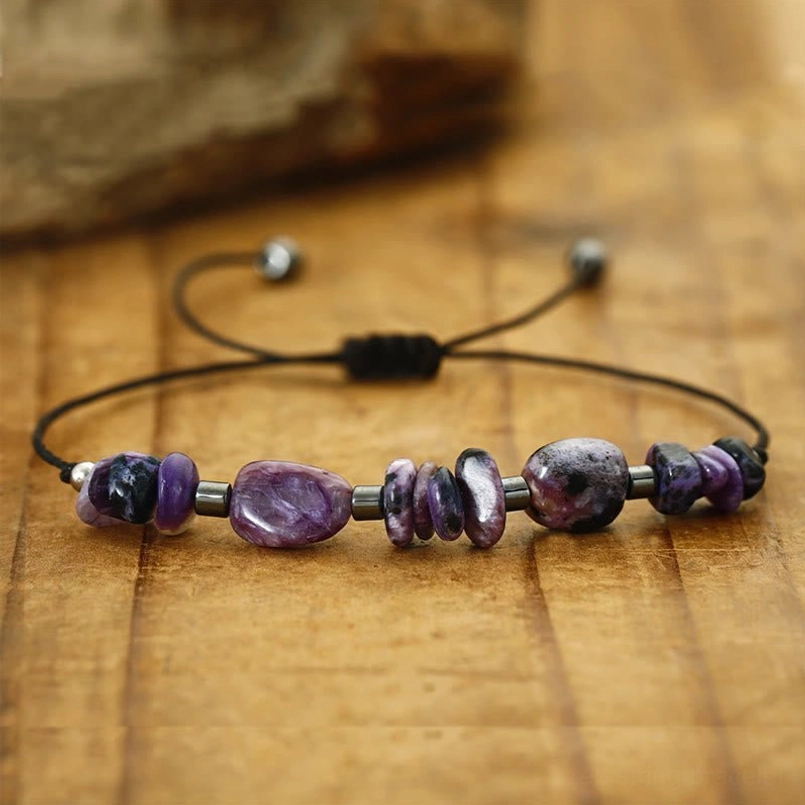 Close-up of charoite and hematite beads with adjustable red cord closure on natural stone background