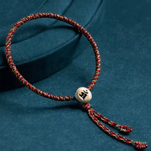 Chinese zodiac natal Buddha protection bracelet with multicolor rope and silver charm pendant on dark teal background