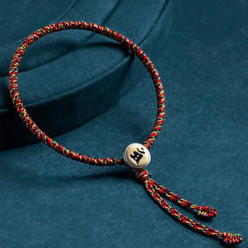 Chinese zodiac natal Buddha protection bracelet with multicolor rope and silver charm pendant on dark teal background