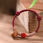 Chinese zodiac red string peach pit cinnabar luck bracelet front view with ancient books and botanical setting